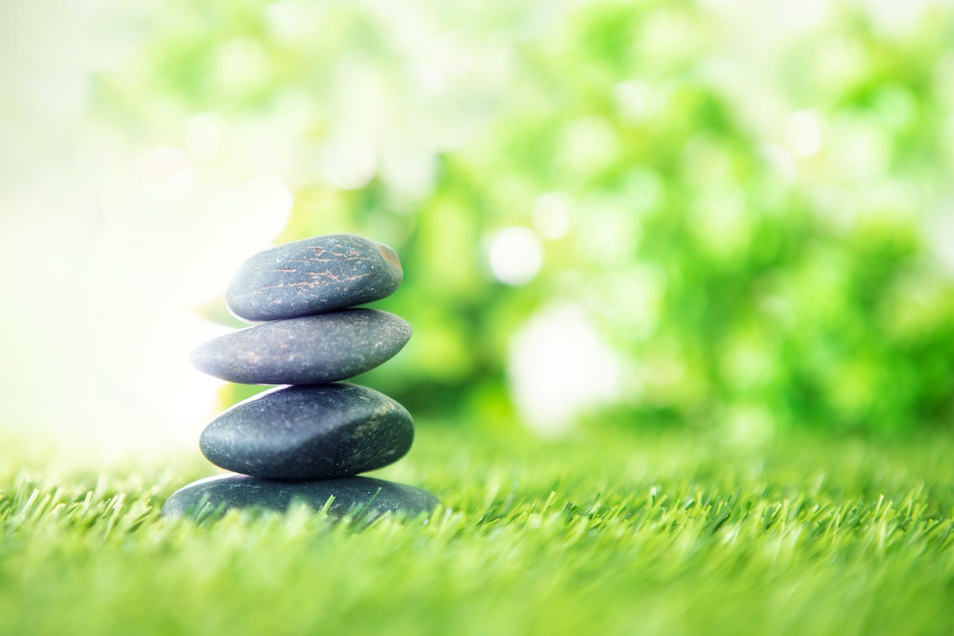 Four smooth stones stacked on grass with a blurred green background, creating a serene and balanced scene.